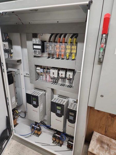 Open electrical control panel showing wiring, circuit breakers, relays, and variable frequency drives inside a metal enclosure.
